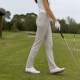 Woman golfer walking on a practice range in neutral golf pants.